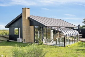 A modern house with a large glass conservatory, a brick chimney, and a well-maintained lawn.