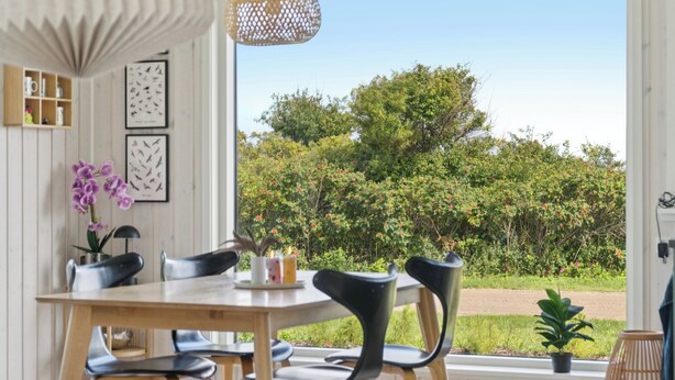 Un coin repas avec une table en bois, des chaises noires et une vue sur la verdure grâce à une grande fenêtre.