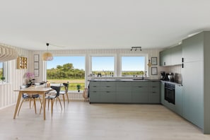 A modern kitchen with a large island, a dining area with chairs, and large windows offering a view of greenery.