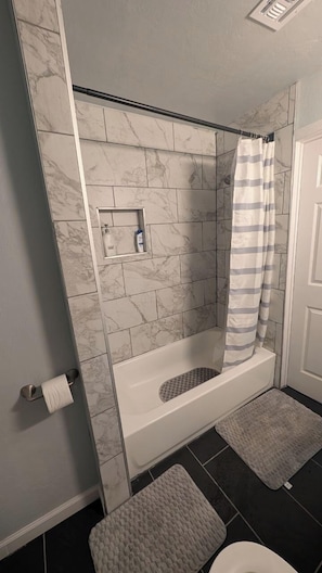 Une salle de bain avec une baignoire, un rideau de douche, un porte-rouleau de papier toilette et une petite étagère contenant des articles de toilette.