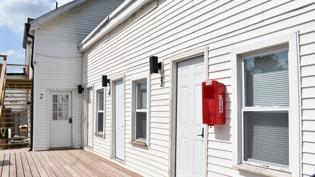 Un bâtiment blanc doté d’une terrasse en bois, d’un système d’alarme incendie et d’un panneau indiquant le numéro « 2 ».