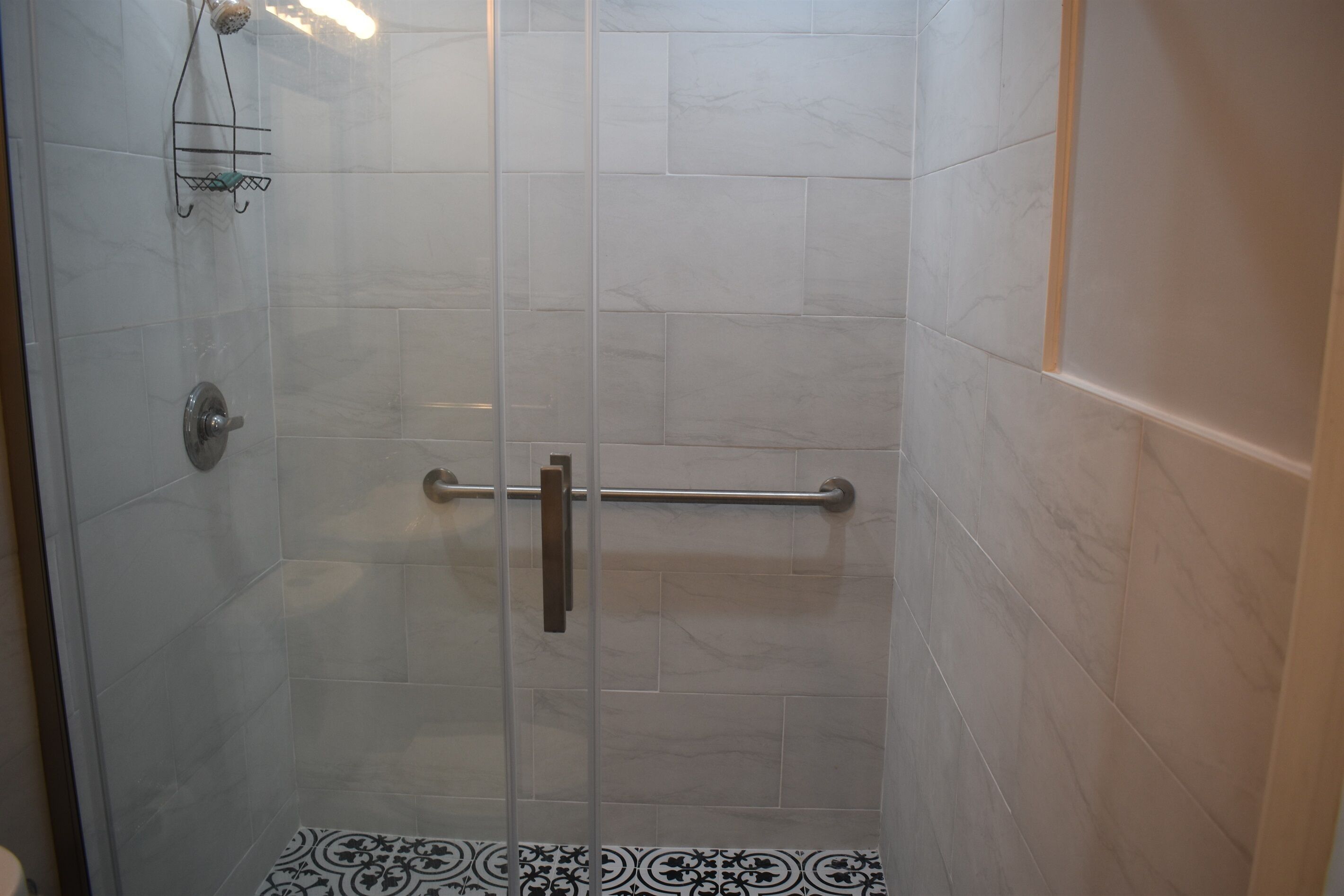 A shower with a glass door, a handrail, and a wall-mounted towel rack.