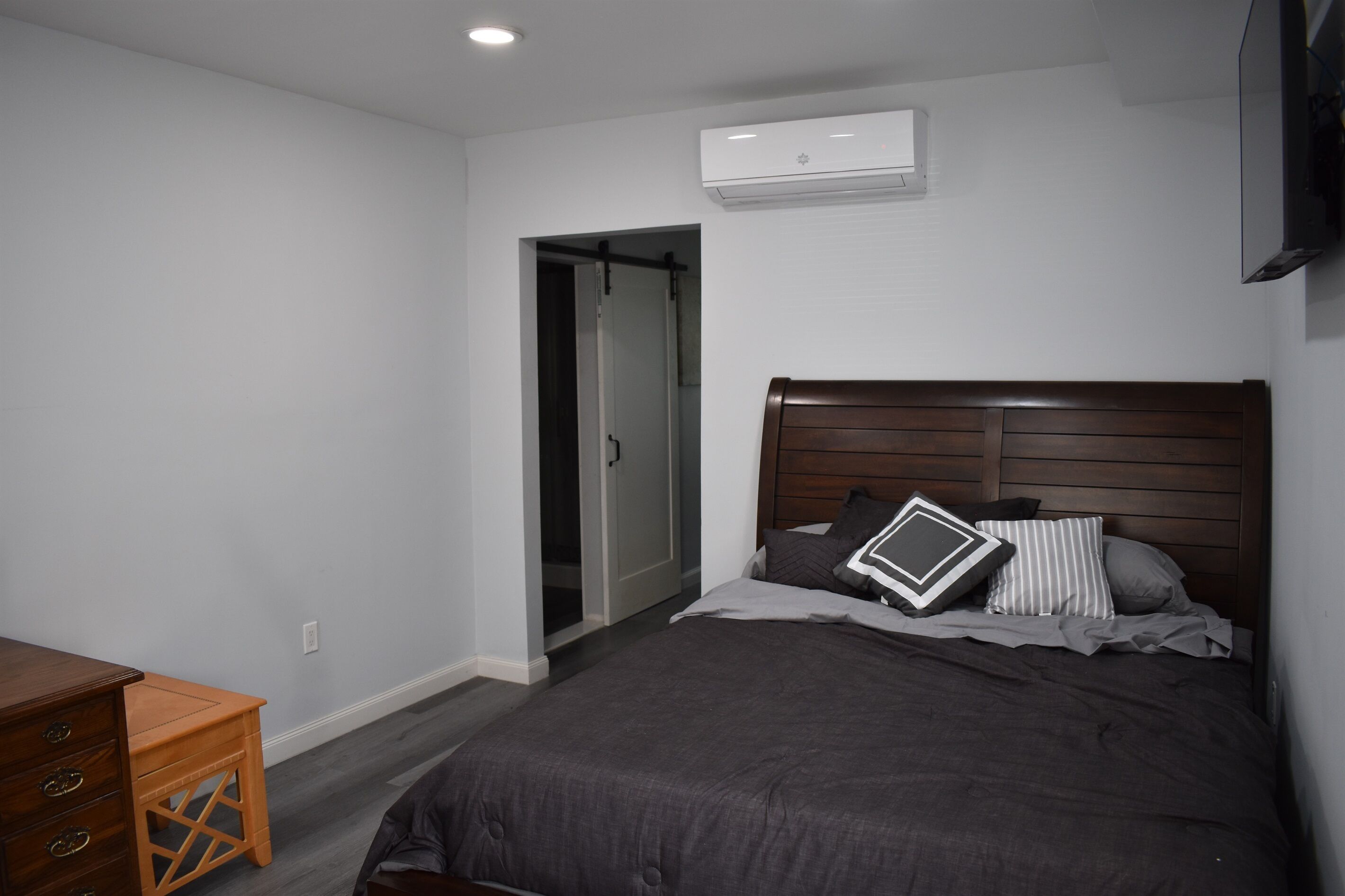Een slaapkamer met een bed, een houten dressoir en een deur naar een andere kamer.