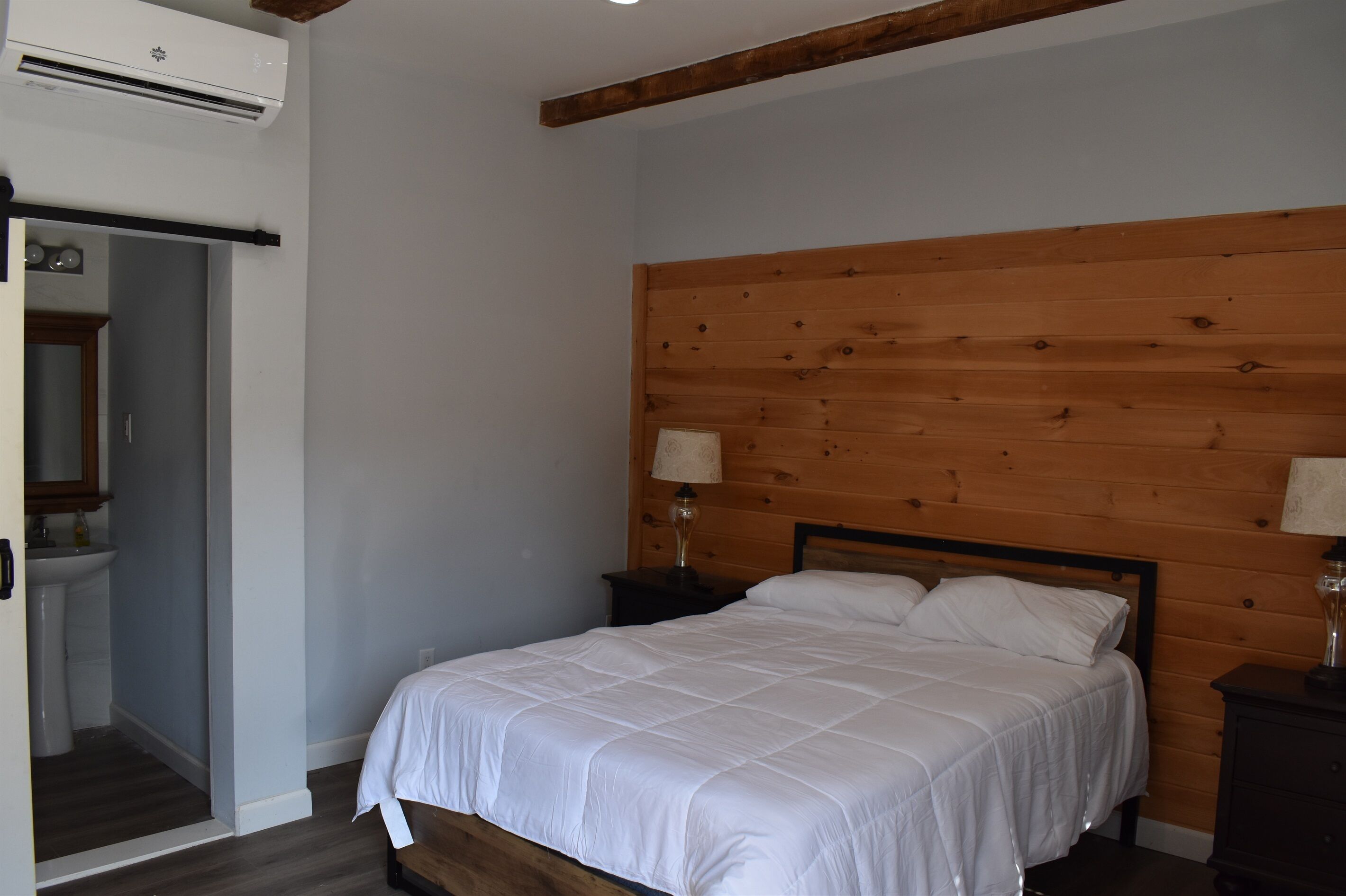 Un dormitorio con cabecera de madera, una cama con ropa de cama blanca, dos lámparas de noche y una mesita de noche pequeña.