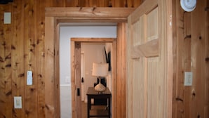 A wooden hallway with a door leading to a room with a table and a lamp.