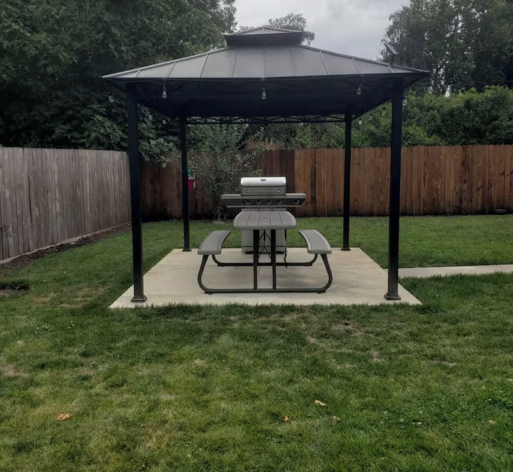 Un jardin avec une table de pique-nique couverte et un espace barbecue.