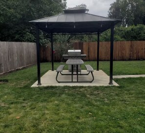 A backyard with a covered picnic table and grill area.