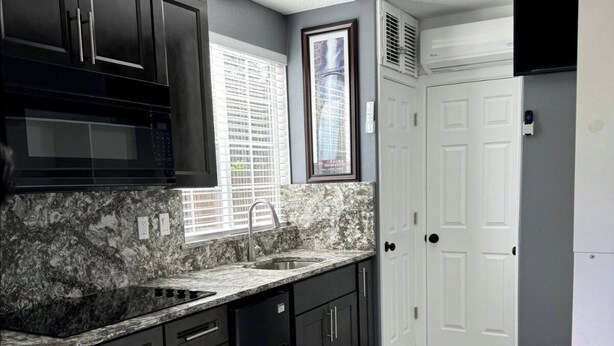 A modern kitchen with dark cabinetry, a granite countertop, and a built-in microwave. - Micro Studio With Outdoor Space Near Nike & Intel (Beaverton)