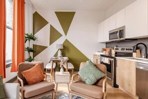 A modern living room with two leather armchairs, a small table, and a kitchen area with a microwave and stove.