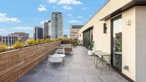 A rooftop terrace with outdoor seating, a wooden deck, and a city skyline view.
