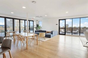 A spacious room with a wooden floor, a dining table with chairs, a sofa, and a balcony with outdoor seating.