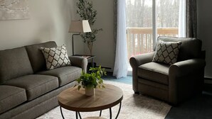A living room with a sofa, armchair, round coffee table, and a potted plant.