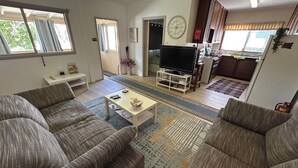 A living room with a sofa set, a coffee table, a TV, and a kitchen area in the background. - Mulberry Cottage: relaxing times with friends, family - and fishing! (Leeman)