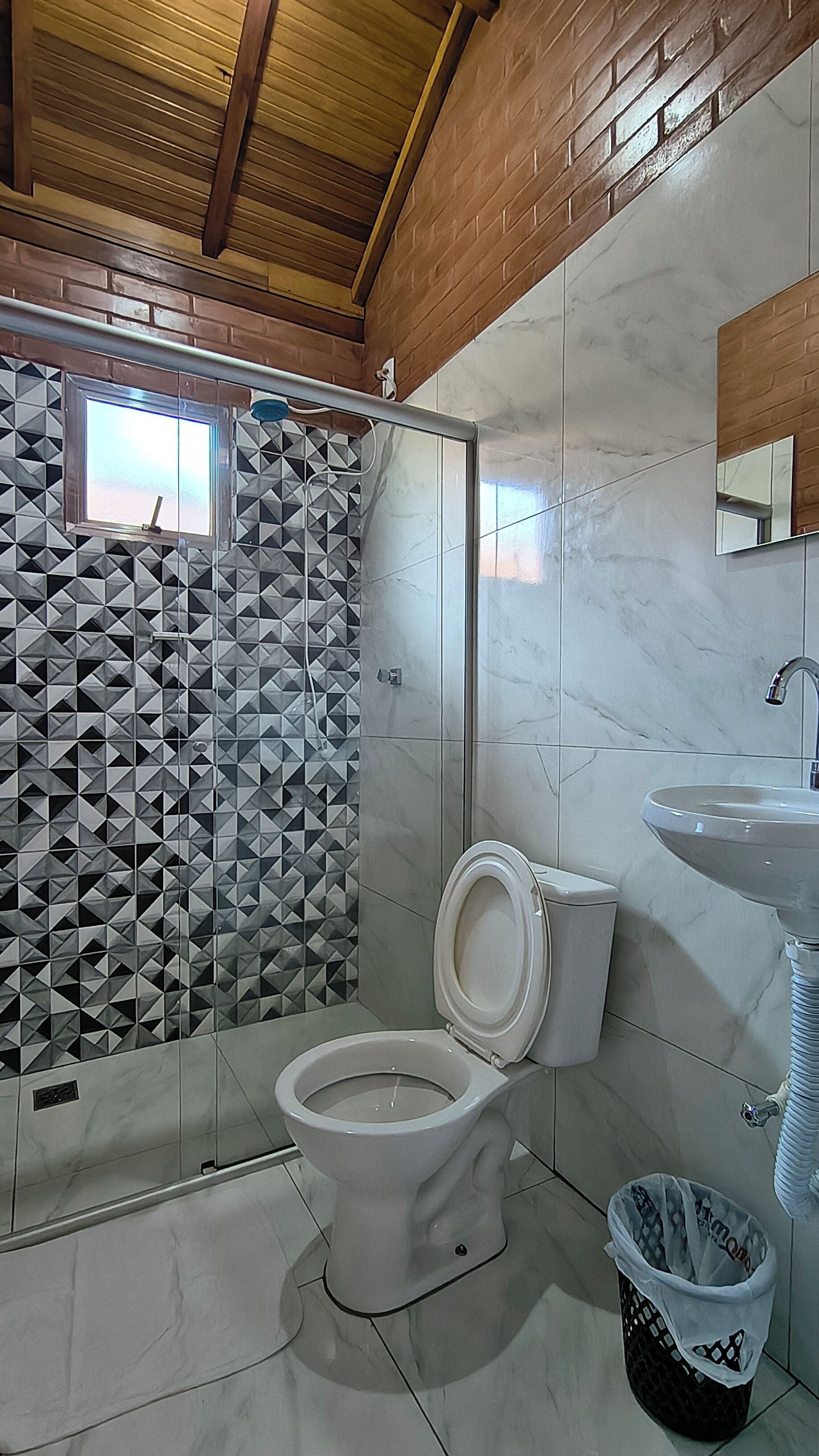 A bathroom with a shower, toilet, sink, and a trash bin.