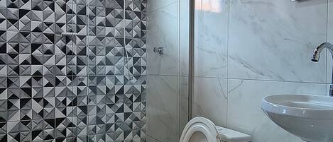 A bathroom with a shower, toilet, sink, and a trash bin.