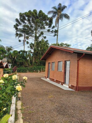 A small brick building with a red roof, a gravel driveway, and a garden with yellow flowers.