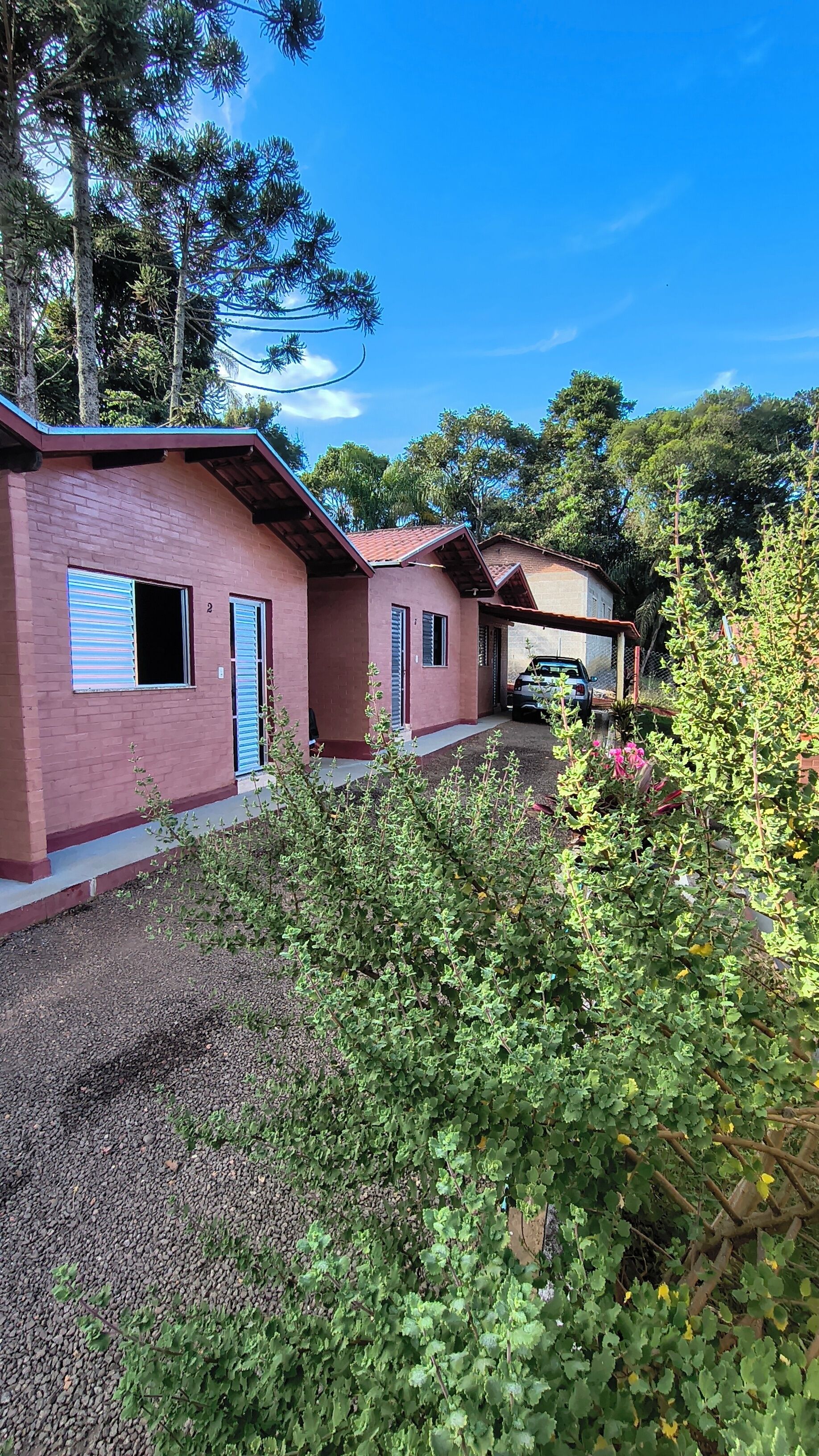 Edificio de dos pisos con fachada de ladrillo rojo, un patio cubierto y un vehículo estacionado al fondo.