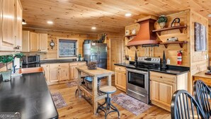 A wooden cabin interior with a kitchen featuring a stove, refrigerator, and wooden cabinets. - Blue Ridge Shadows Lodge: Escape to the serene Blue Ridge Mountains (Morganton)