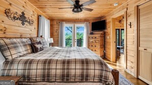 A wooden cabin bedroom with a plaid bedspread, a ceiling fan, a dresser, and a TV on the wall. - Blue Ridge Shadows Lodge: Escape to the serene Blue Ridge Mountains (Morganton)