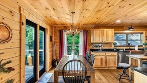 A wooden cabin interior with a dining table, chairs, a chandelier, wooden cabinets, and a kitchen area. - Blue Ridge Shadows Lodge: Escape to the serene Blue Ridge Mountains (Morganton)