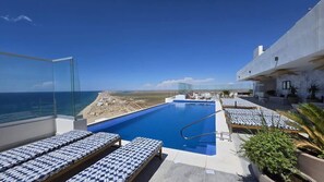 A rooftop infinity pool with lounge chairs, a clear view of the beach, and a modern building structure. - Beachfront Luxury Condo w/ Infinity Pool & Hot Tub (Playa Encanto)