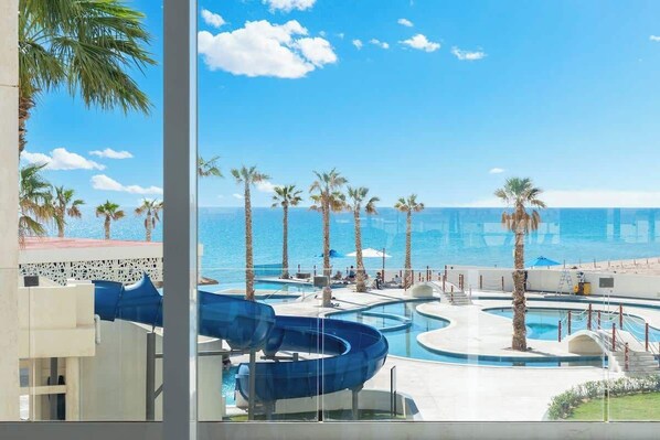 A pool area with multiple water slides and palm trees, overlooking a beach.