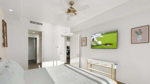 A hotel room with a bed, a ceiling fan, a TV on the wall, and a small cabinet.