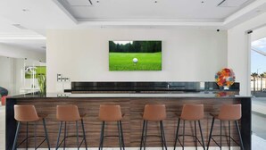 A modern kitchen with a central island, bar stools, a flat-screen TV, and a vase with flowers.