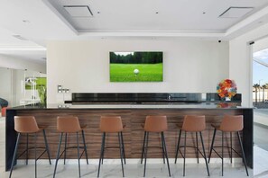 A modern kitchen with a central island, bar stools, a flat-screen TV, and a vase with flowers. - Beachfront Luxury Condo w/ Infinity Pool & Hot Tub (Playa Encanto)