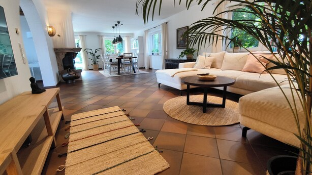 A spacious living room with a large sofa, a coffee table, and a wooden bench. There is a dining area with chairs and a table in the background. - Vacation home Fringaluna with private pool in Übersee am Chiemsee (Übersee)
