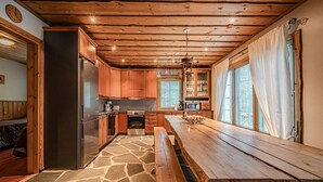 A kitchen with wooden cabinets, a stone-patterned floor, a wooden bench, and a view through the window.