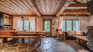 A rustic cabin interior with a stone floor, wooden furniture, and a stone fireplace.