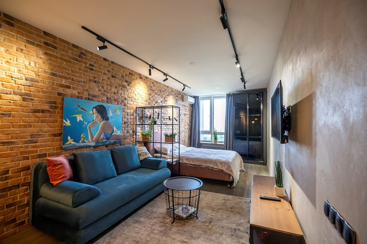 A modern room with a brick wall, a blue sofa, a bed, a small table, and a painting.