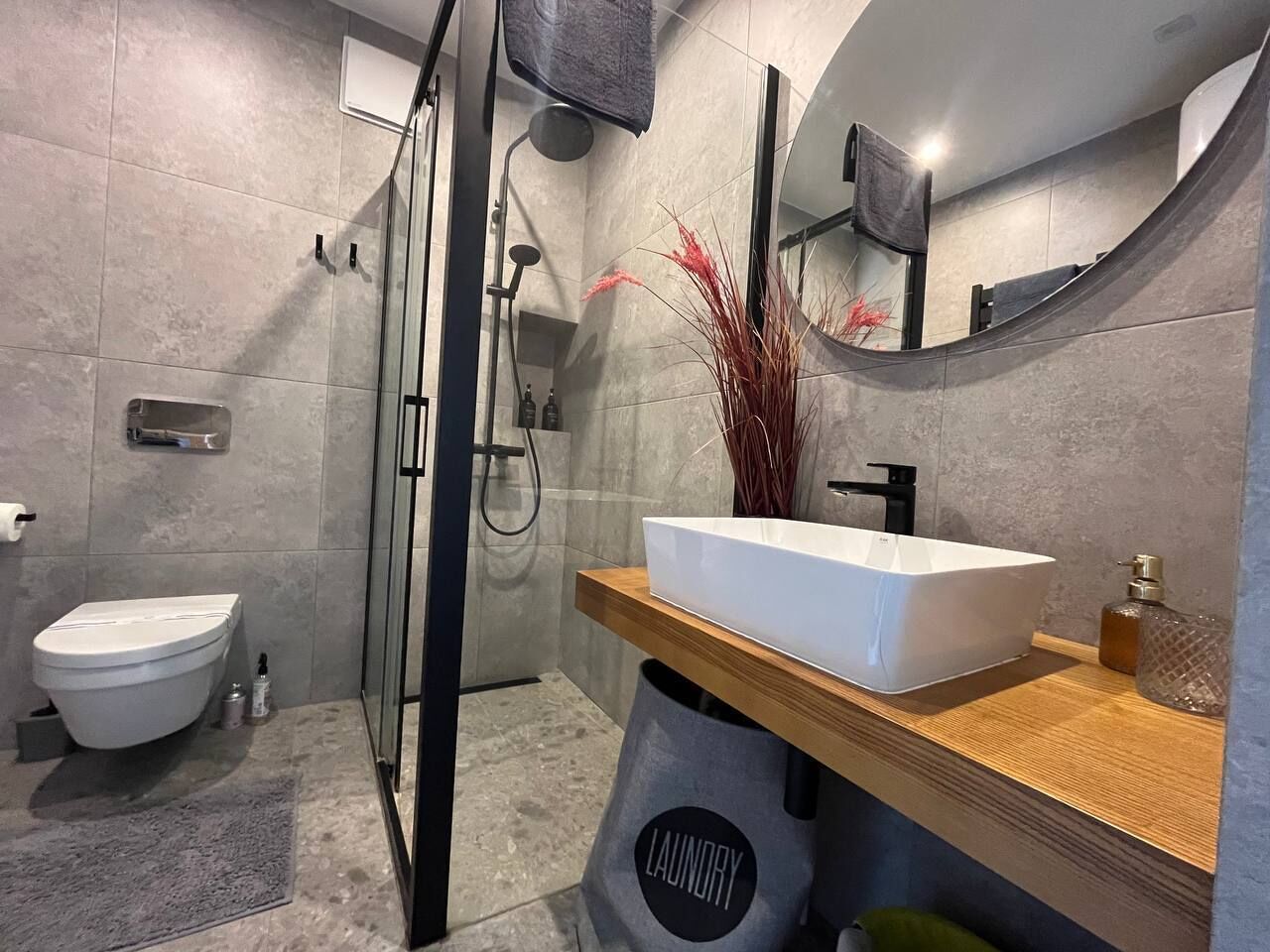 A modern bathroom with a glass-enclosed shower, a white sink on a wooden countertop, and a toilet.