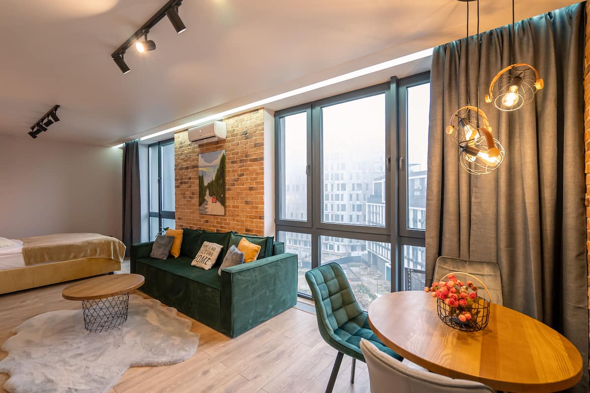A modern living room with a green sofa, a wooden dining table, and a large window with a city view.