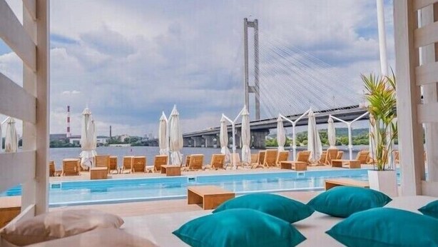 Un espace aménagé au bord de la piscine, avec des chaises longues et des parasols, une vue sur un pont et un ciel dégagé.