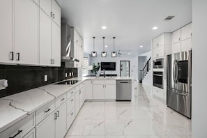 A modern kitchen with white cabinetry, a central island, stainless steel appliances, and pendant lighting.