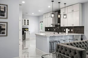A modern kitchen with white cabinets, a central island with bar stools, and pendant lighting.