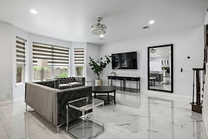 A modern living room with a sectional sofa, a glass coffee table, and a flat-screen TV mounted on the wall.