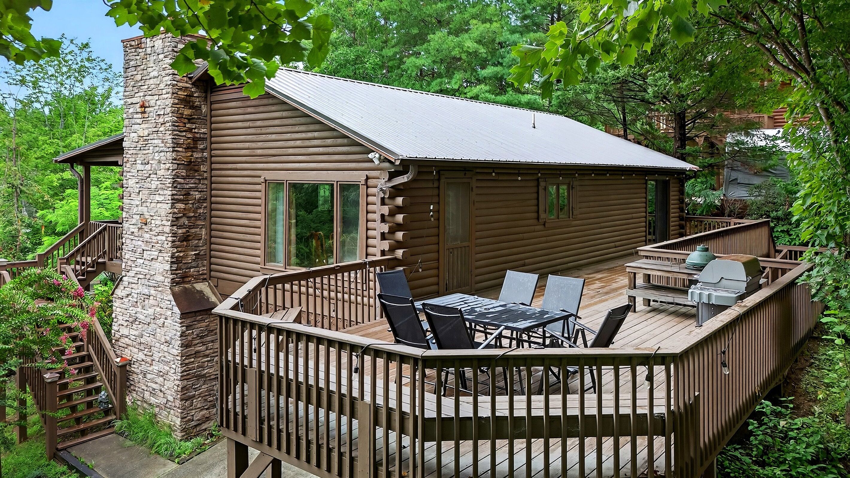 A log cabin with a deck, outdoor seating, and a stone chimney.