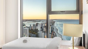 Une chambre d’hôtel dotée d’une grande fenêtre donnant sur le panorama de la ville et sur la plage.