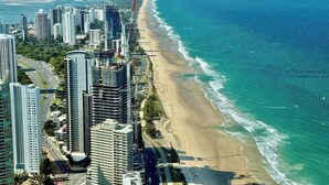 A coastal cityscape with high-rise buildings, a beach, and a clear blue sky.