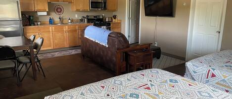A hotel room with a kitchenette, a TV, a bed with patterned bedding, and a brown leather sofa.