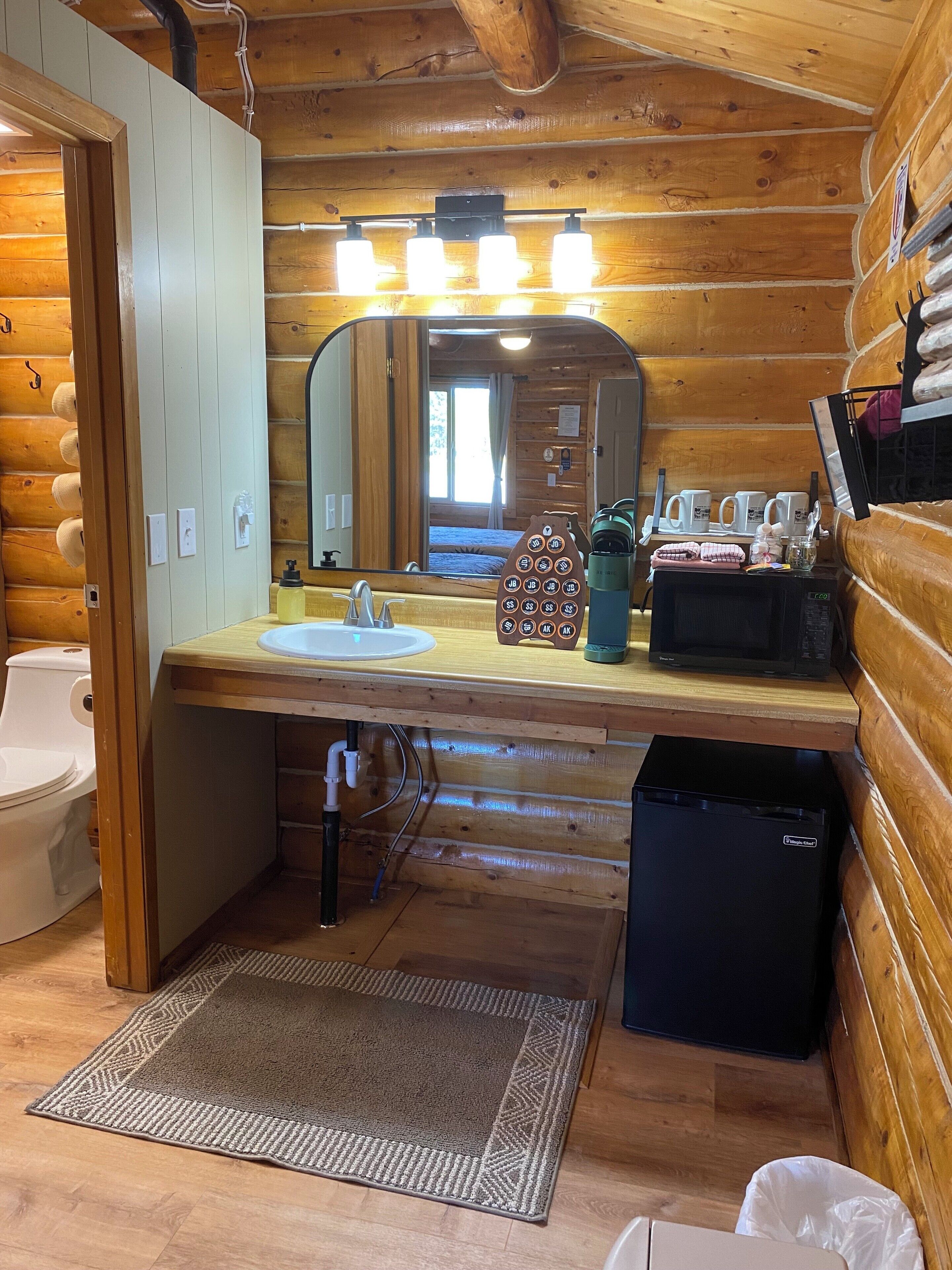 Une salle de bain rustique, aménagée dans une cabane en bois, avec un lavabo, un miroir et des toilettes.