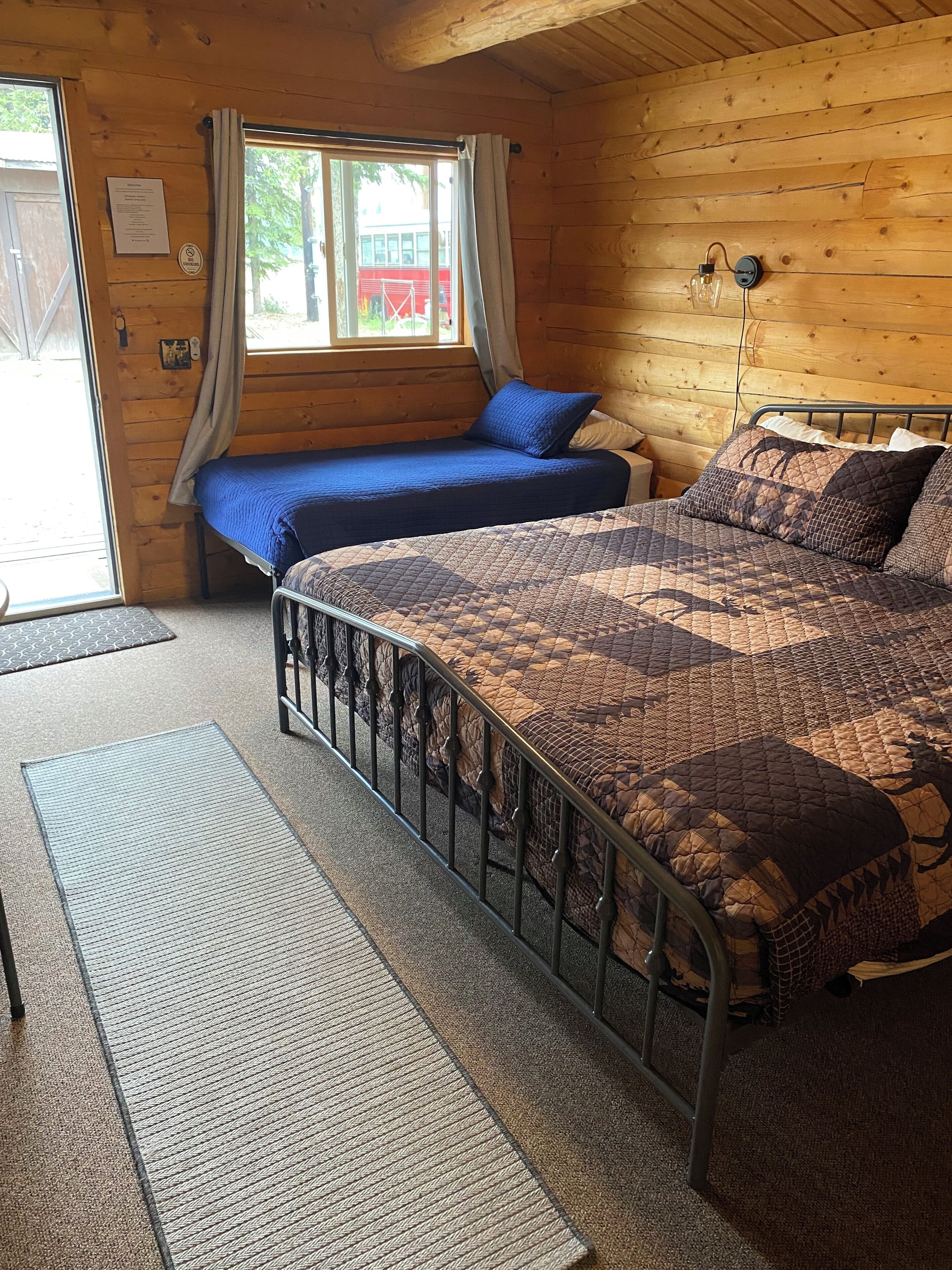 Un dormitorio tipo cabaña de madera con dos camas, una con cubrecama azul y la otra con colcha estampada.