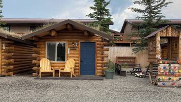 Una cabaña rústica de troncos con puerta azul, número 2, y dos sillas Adirondack de madera frente a ella.