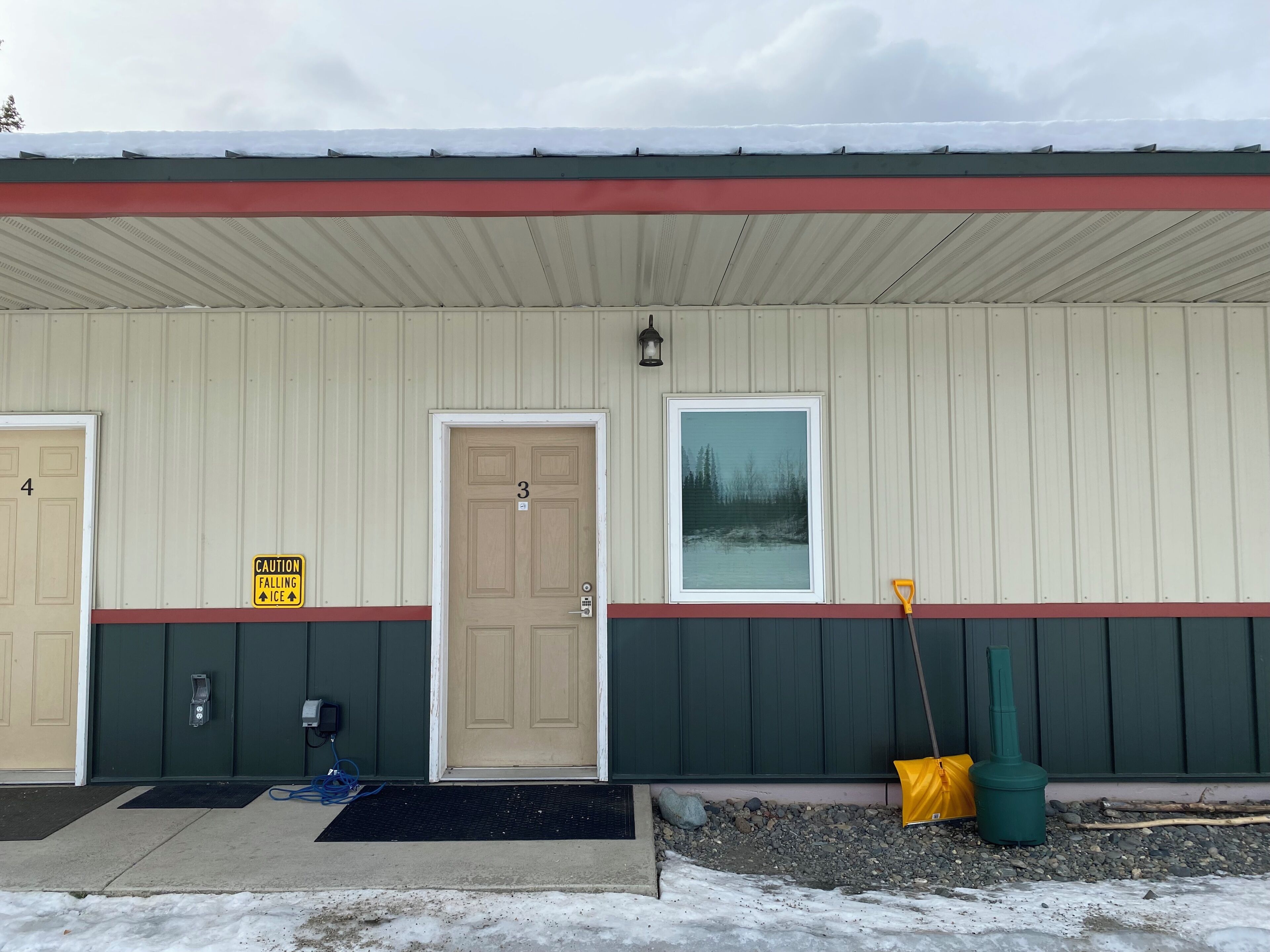 Un bâtiment avec trois portes, un panneau d’avertissement, une fenêtre et des outils de nettoyage pour l’extérieur.