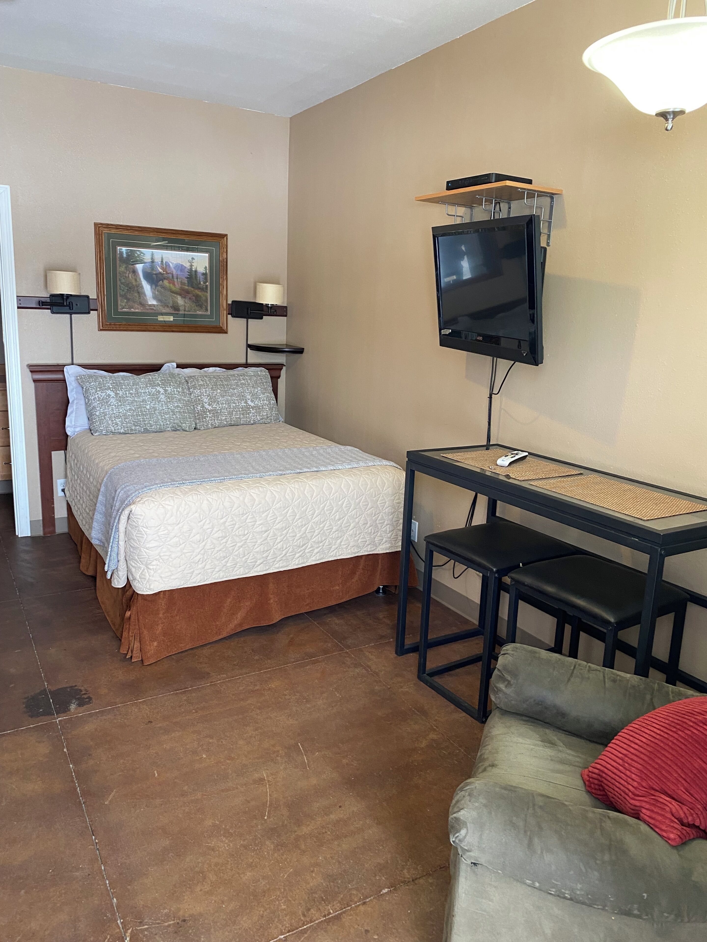 A room with a bed, a TV, a desk with chairs, and a couch.