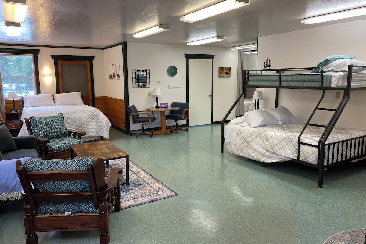 A dormitory room with bunk beds, a desk, chairs, and a small table.