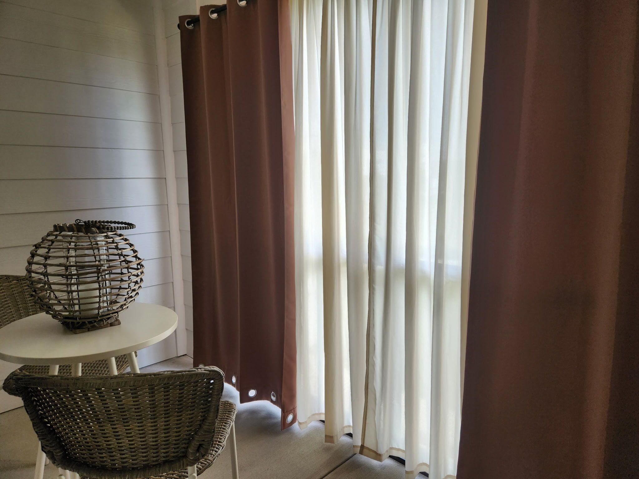 A room with a round table, wicker chairs, a decorative glass lamp, and a window with brown curtains.